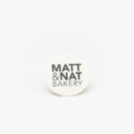 A Round Celebration Logo Disc with a Matt & Nat Bakery Logo on a light grey background