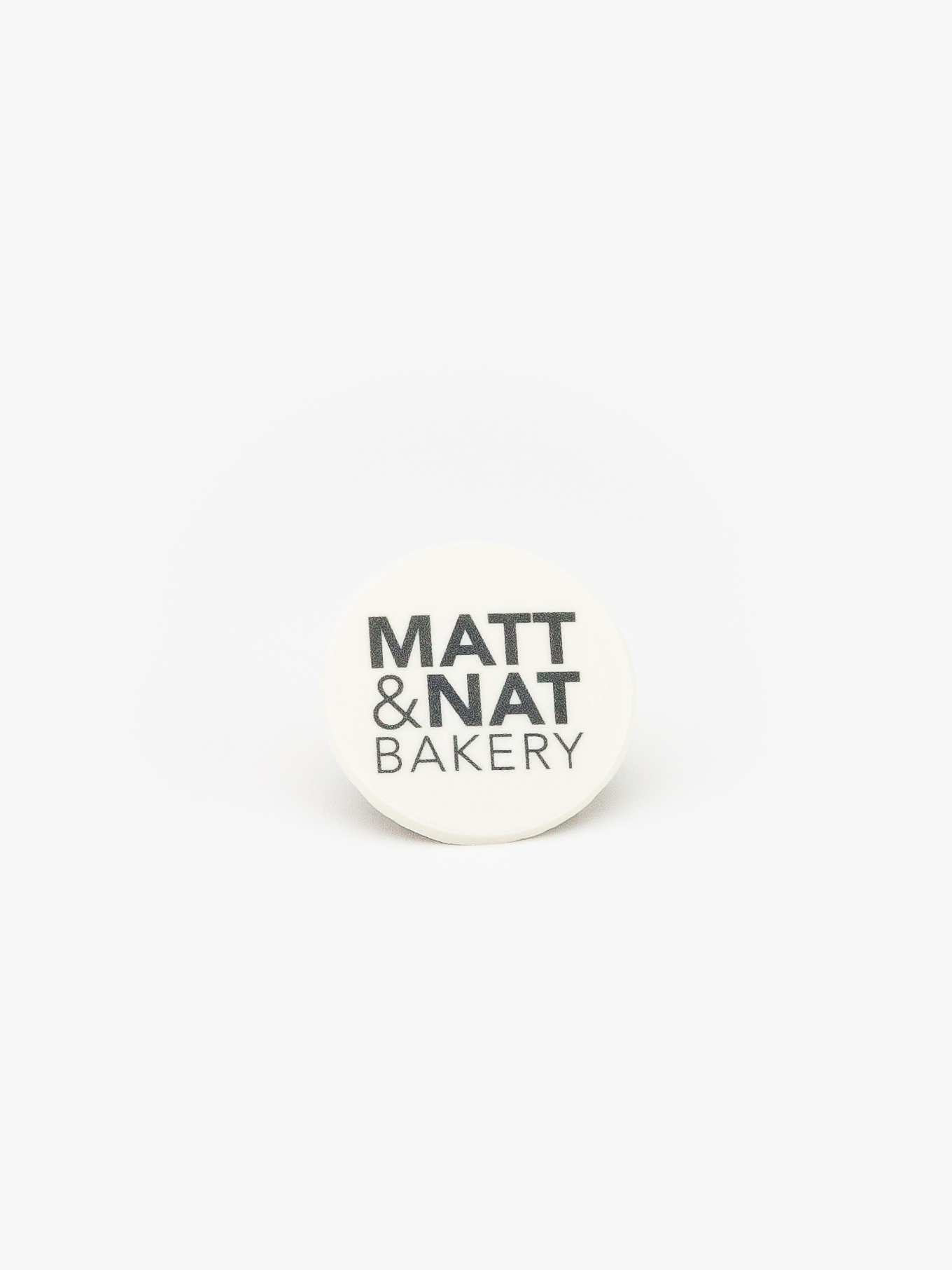 A Round Celebration Logo Disc with a Matt & Nat Bakery Logo on a light grey background