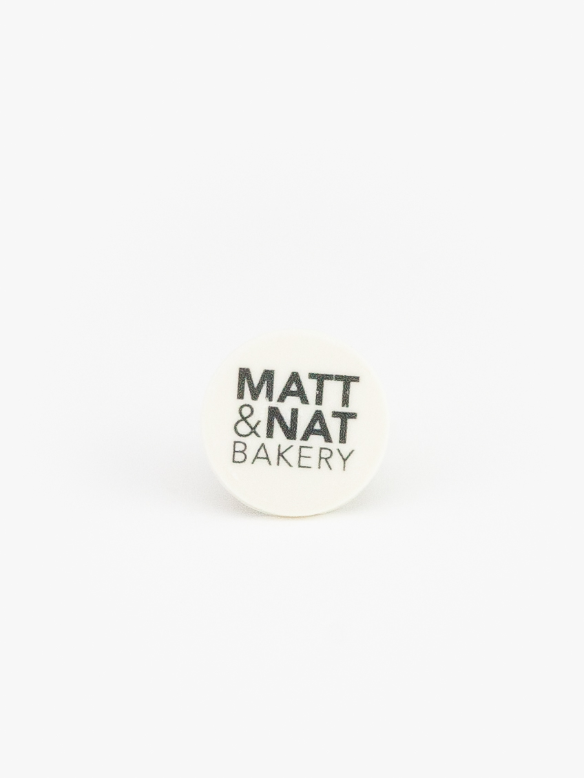 A Round Celebration Logo Disc Topper with a Matt & Nat Bakery Logo on a light grey background