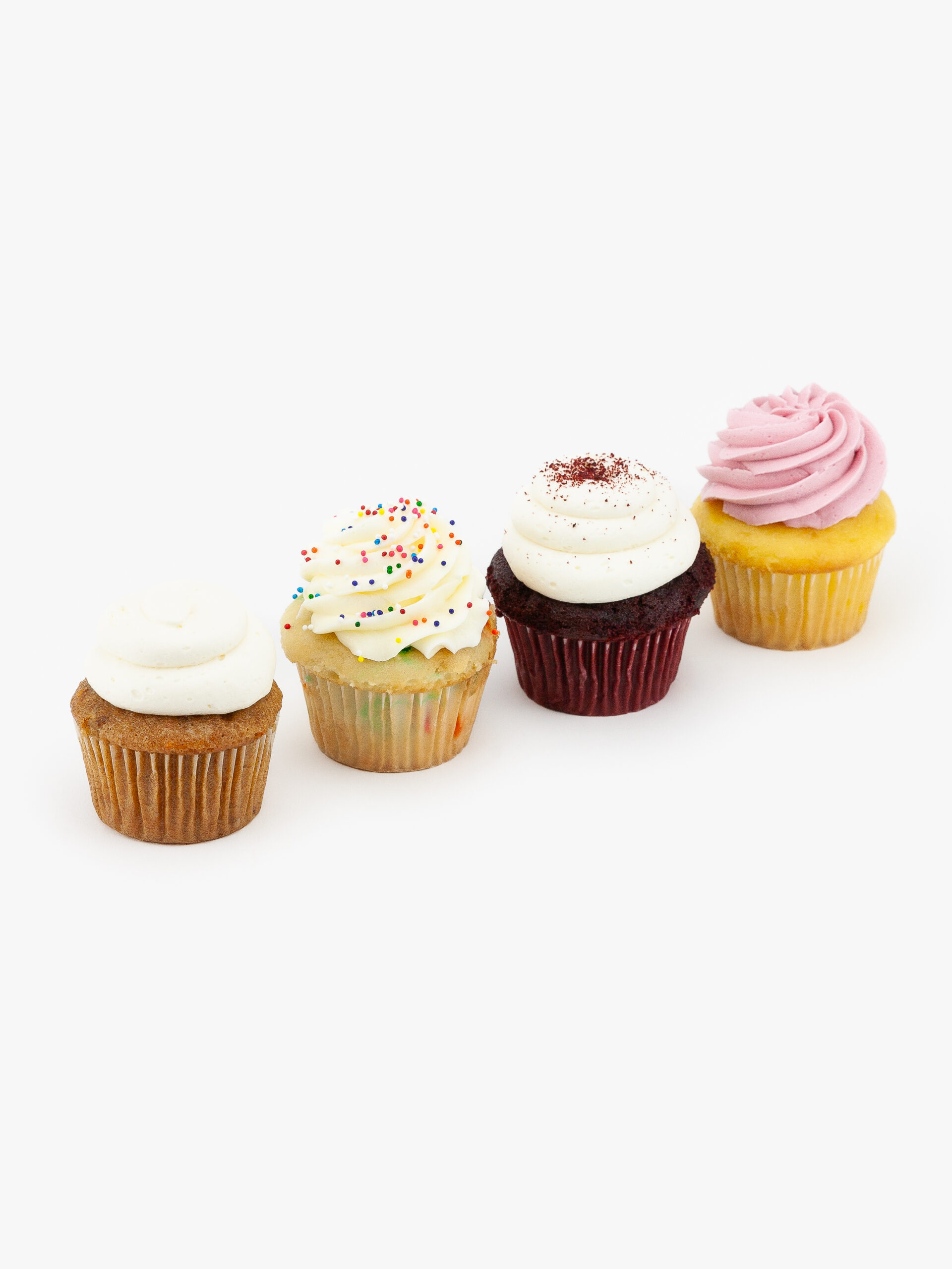 4 Regular Deluxe Assorted Dessert Cupcakes in wrapping on a light grey background