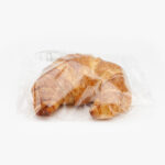 An Individually Wrapped Jumbo Butter Croissant in recyclable material on a light grey background