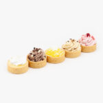 Assorted Mini Dessert Tarts, Lemon, Raspberry Mousse, Dulce De Leche, Chocolate Mousse and Custard Cream on a light grey background.